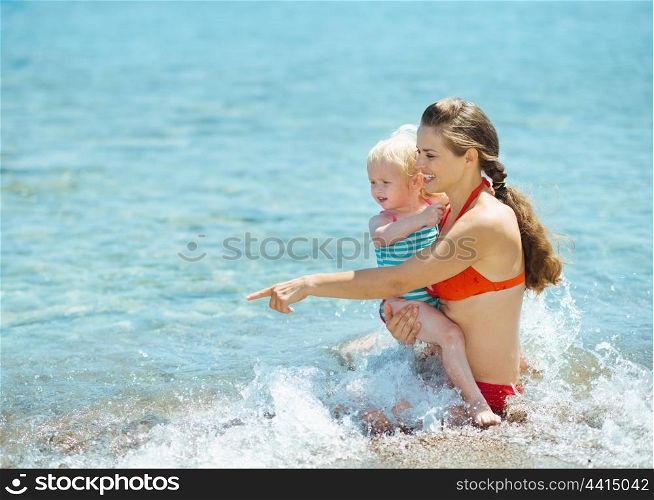 Mother showing something to baby girl at seaside