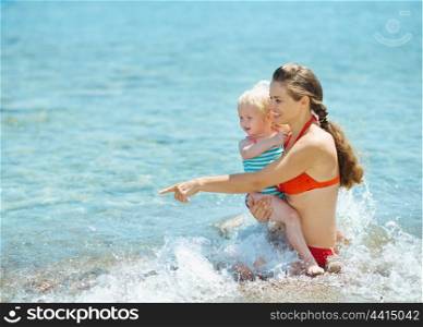 Mother showing something to baby girl at seaside