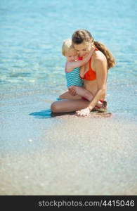 Mother showing something to baby girl on sea coast