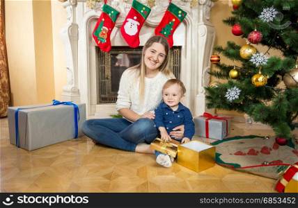 Mother siting on floor with baby son at living room decorated for Christmas