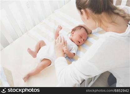 Mother sitting near the cradle and holding baby&rsquo;s hand