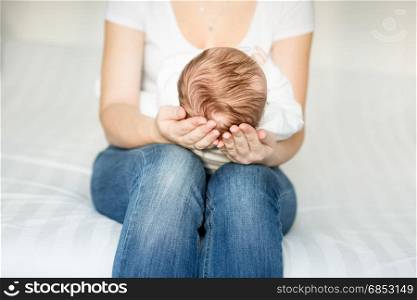 Mother sitting on bed and holding head of her 3 months old baby
