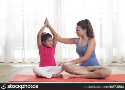 Mother sitting on floor teaching yoga to daughter
