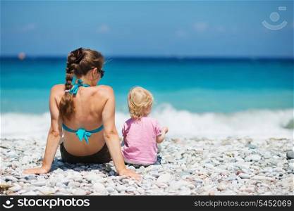 Mother sitting with baby on beach. Rear view