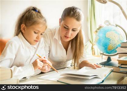 Mother sitting with daughter at desk and explaining complicated task at homework