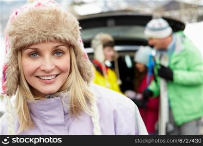 Mother Smiling At Camera Whilst Family Load Skis In Boot Of Car