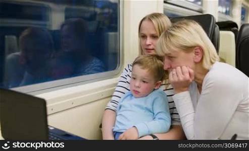 Mother, son and grandmother watching video on laptop in the train