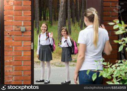 Mother standing in house yard and waving to her daughters walking to school