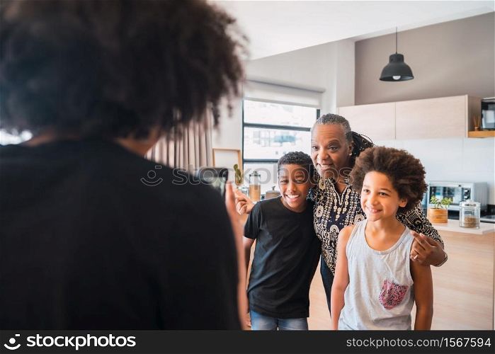 Mother taking a photo of grandmother with her grandchildren at home. Family and lifestyle concept.