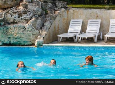 Mother teaches children to swim in the summer outdoor pool.