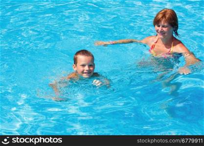 Mother teaches her son to swim in the summer outdoor pool.