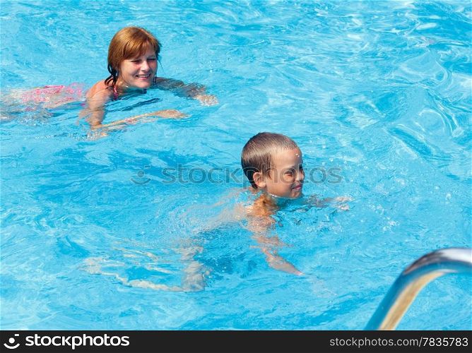 Mother teaches her son to swim in the summer outdoor pool.