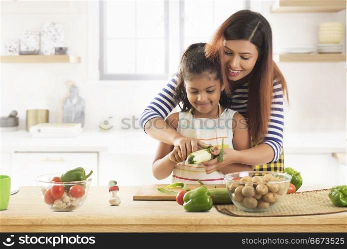 Mother teaching daughter how to peeling cucumber in kitchen