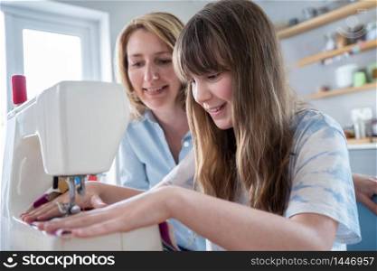 Mother Teaching Daughter How To Use Sewing Machine At Home