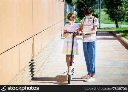 Mother teaching her daughter to ride an electric scooter in urban background wearing surgical masks. Mother teaching her daughter to ride an electric scooter