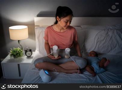 mother using breast pump machine to pumping milk while talking with her newborn baby on a bed at night