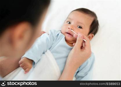 mother using cotton bud to clean nose of newborn baby on a bed