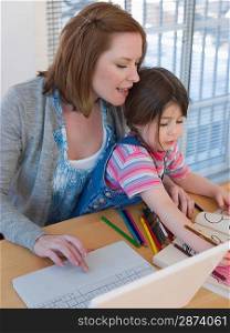 Mother Using Laptop While Daughter Colors