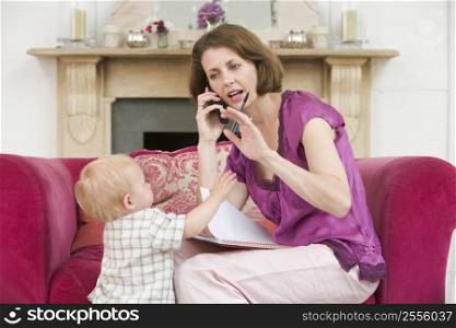 Mother using telephone in living room with baby frowning
