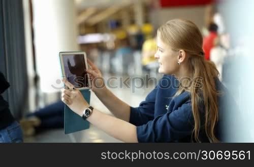 Mother using touch pad to take pictures of her little son watching out the window in the waiting room