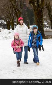 Mother Walking Two Children To School Along Snowy Street In Ski Resort