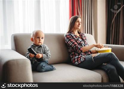 Mother watch tv, little male kid plays near. Mom and son happy together at home, togetherness