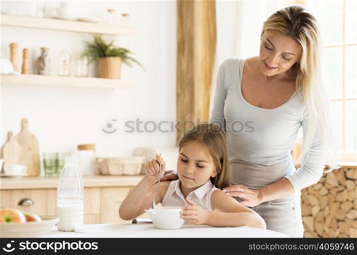 mother watching her daughter eat breakfast
