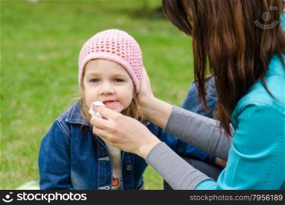 Mother wipes his mouth with a napkin girl on picnic. Young girl and a three year old at a picnic on a green lawn