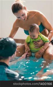 Mother with baby boy and instructor, swimming class, indoor swimming pool