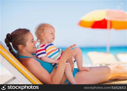 Mother with baby laying on sunbed and pointing on copy space