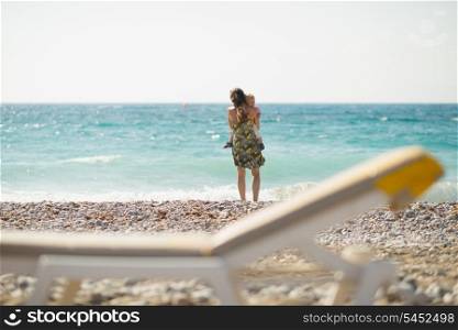 Mother with baby on beach looking into distance. Rear view
