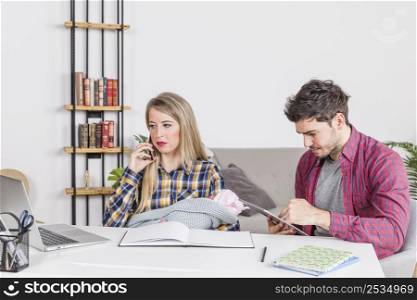 mother with baby talking phone while father using tablet