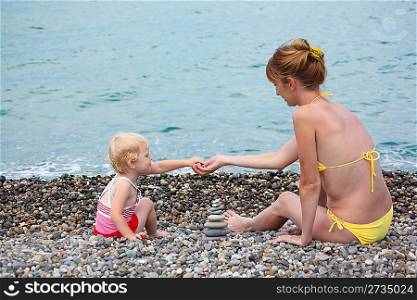 Mother with child on sea coast build pyramid of stones