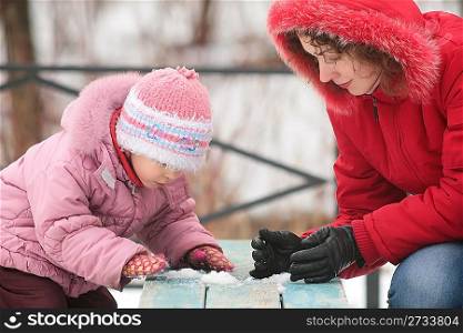 mother with child play with snow on bench