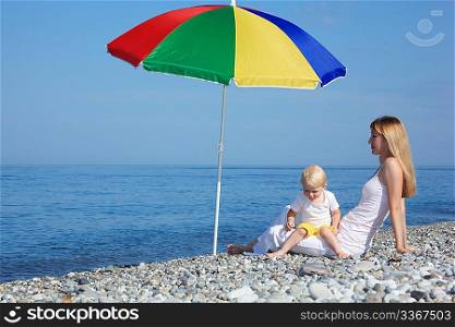 Mother with child under a multi colored umbrella on pebble beach