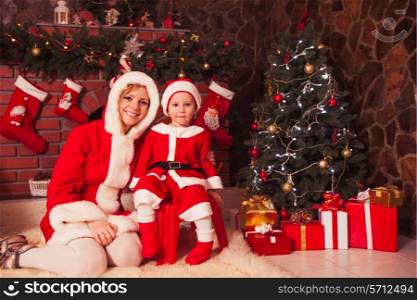 Mother with children are sitting near fireplace and play with cones - Christmas decorations