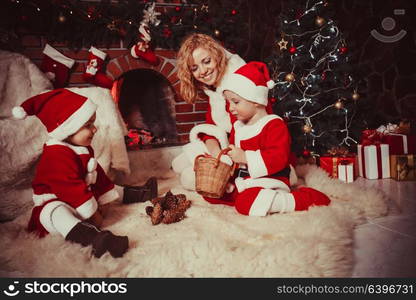 Mother with children are sitting near fireplace and play with cones - Christmas decorations. Christmas decorated fireplace