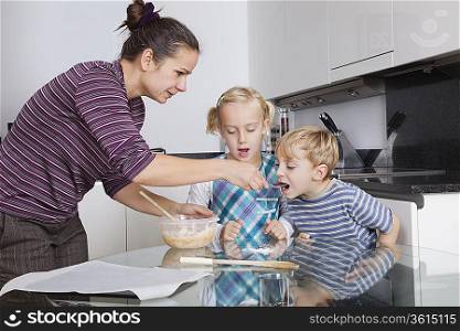 Mother with children baking and tasting cookie batter in kitchen
