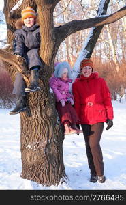 Mother with children on tree in wood in winter