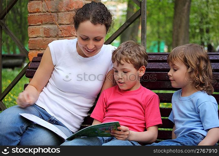 Mother with children sit on bench and read book