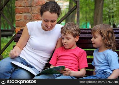 Mother with children sit on bench and read book