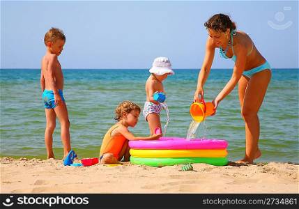 Mother with children to pour water in inflatable pool on shore of sea