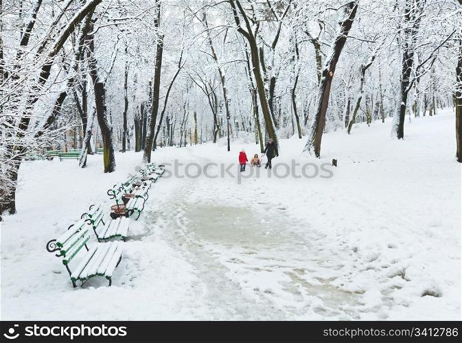 Mother with children walking in winter snow covered city park (dull day)
