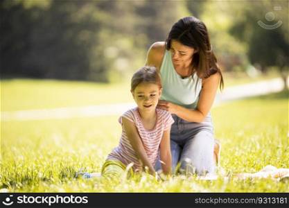 Mother with cute little daughter having fun on the grass at the park