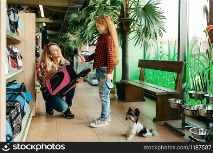 Mother with daughter choosing bag for little puppy in pet store. Woman and little child buying equipment in petshop, accessories for domestic animals. Mother with daughter choosing bag in pet store