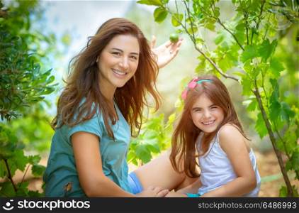 Mother with daughter in the orchard, enjoying the appearance of first fruits, young gardeners with pleasure spending time in the garden, happy life in countryside. Mother with daughter in the orchard