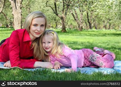 Mother with daughter lie on grass in park in spring