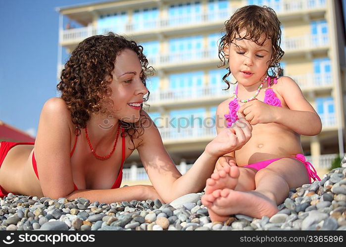 Mother with daughter on pebble in swimwear