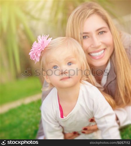 Mother with daughter playing outdoors, lying down on fresh green grass field in the park, happy family spending summer vacation