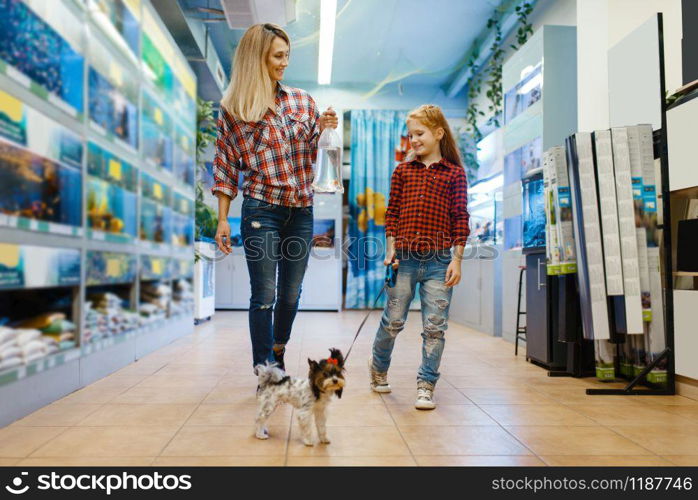 Mother with daughter walking in pet store with little puppy. Woman and little child buying equipment in petshop, accessories for domestic animals. Mother with daughter walking in pet store